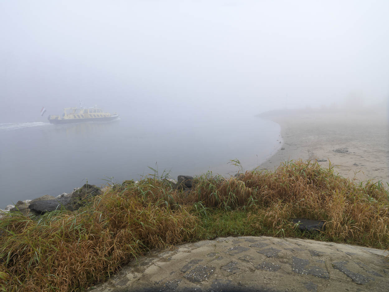 rivier met RWS-schip in de mist
