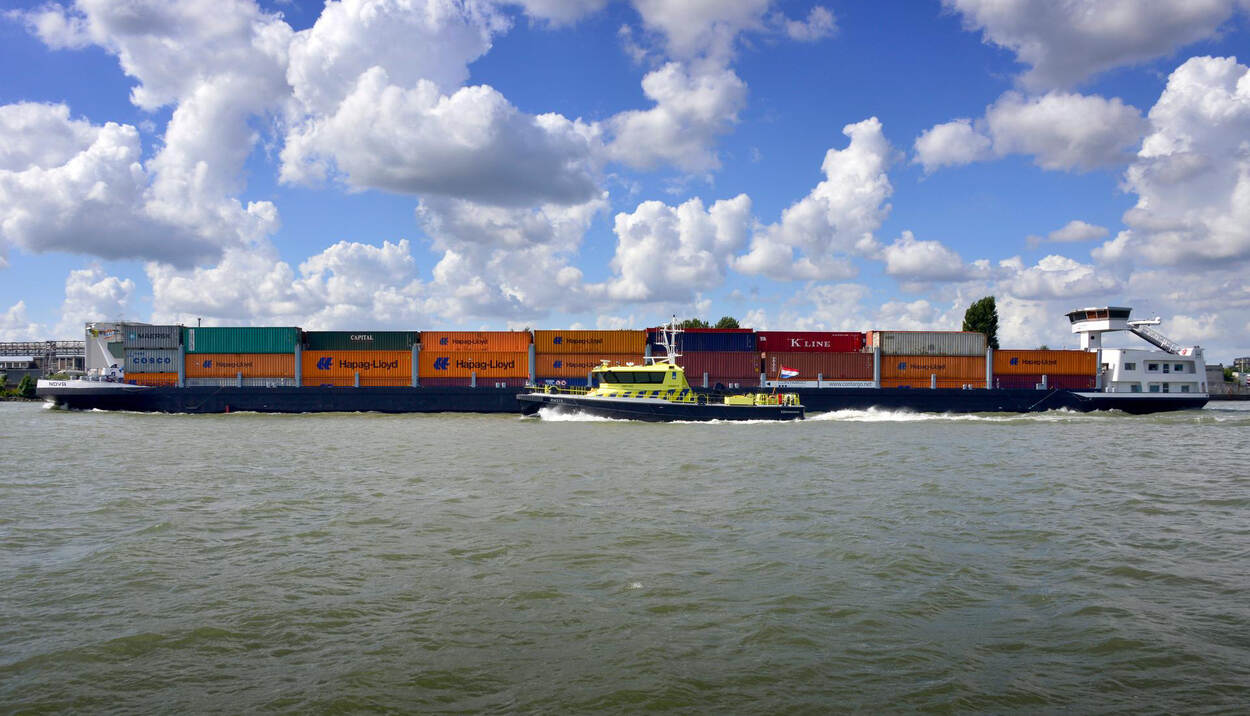 Zijaanzicht containerschip en schip van Rijkswaterstaat.