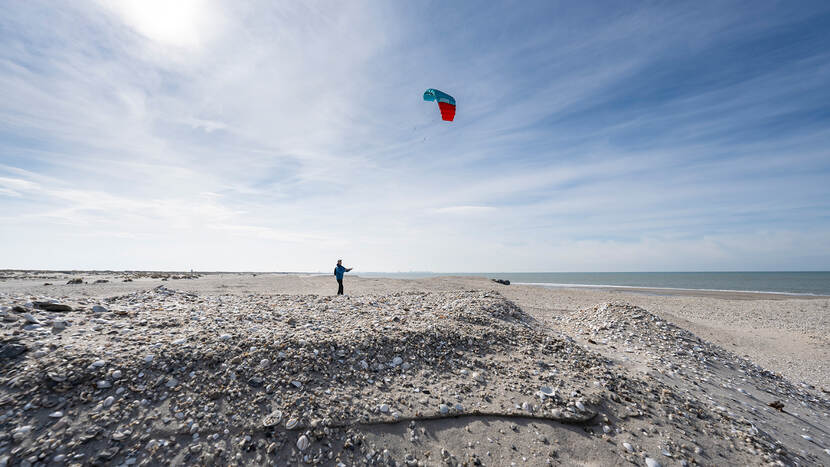 Foto van persoon aan het vliegeren op een opgespoten strand