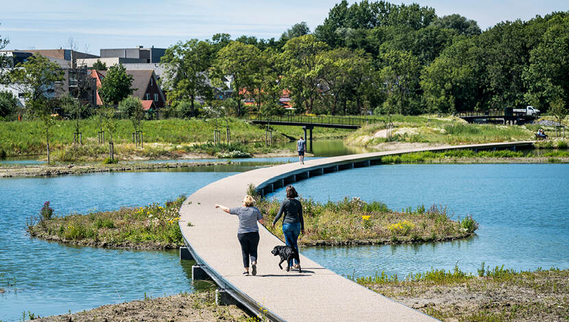 Waterberging in het Molenvlietpark aan de rand van Den Haag. Twee vrouwen met hond lopen over vlonder.