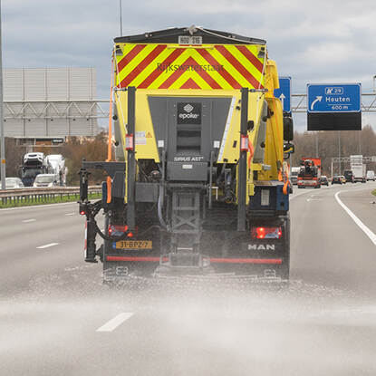Foto van de achterzijde van een strooiwagen die zout strooit op de snelweg