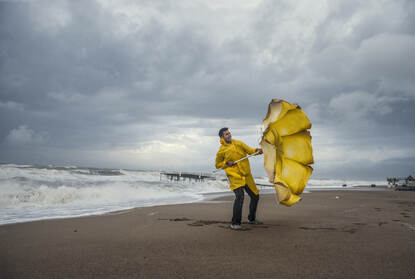 Een man staat op het strand met een dubbel geklapte paraplu
